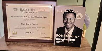 Darius McDougle's Marquis Who's Who certificate beside his ROI: Return On Imagination book